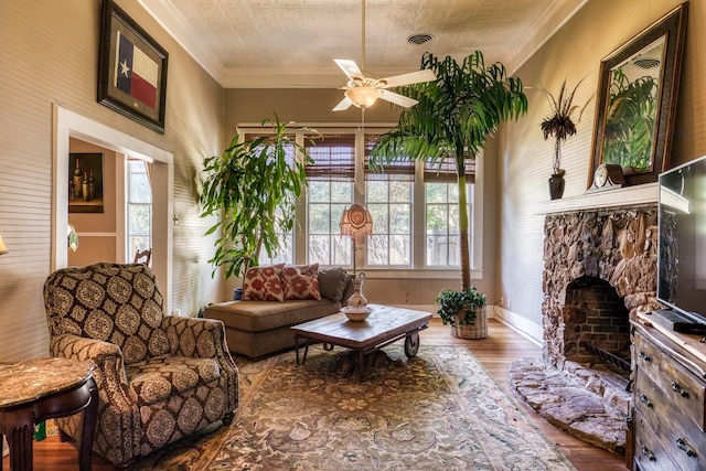 living area with a fireplace, hardwood / wood-style floors, ceiling fan, and crown molding