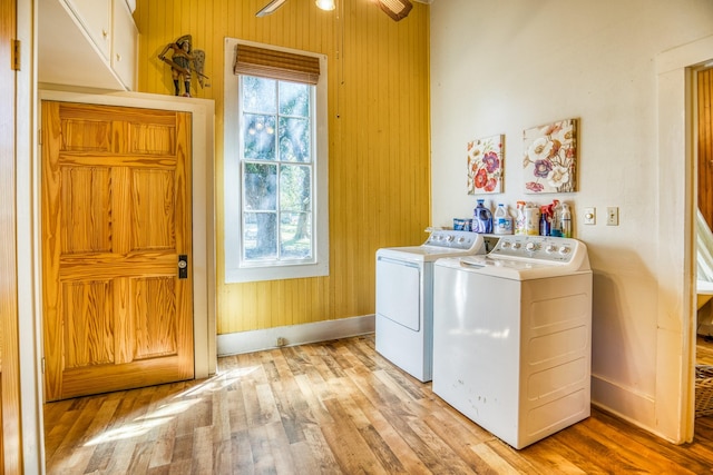 clothes washing area with cabinets, wooden walls, washer and dryer, ceiling fan, and light hardwood / wood-style floors