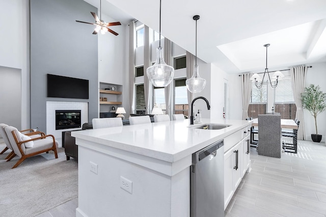 kitchen featuring a kitchen island with sink, white cabinets, sink, stainless steel dishwasher, and a fireplace