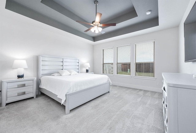 bedroom featuring a raised ceiling, ceiling fan, and light carpet