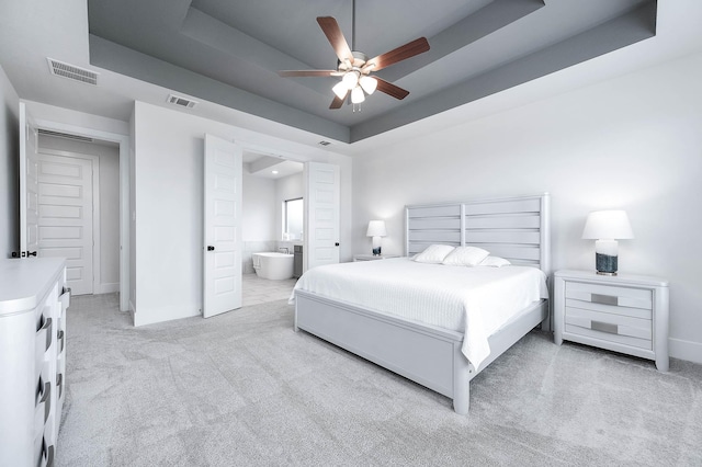 bedroom with ensuite bath, a raised ceiling, ceiling fan, and light colored carpet