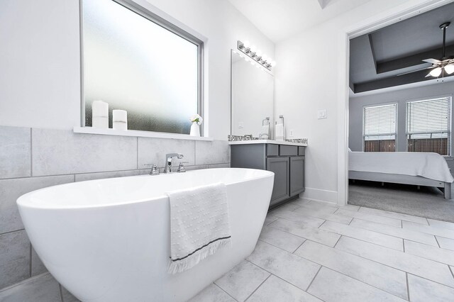 bathroom with ceiling fan, a washtub, tile patterned flooring, vanity, and tile walls