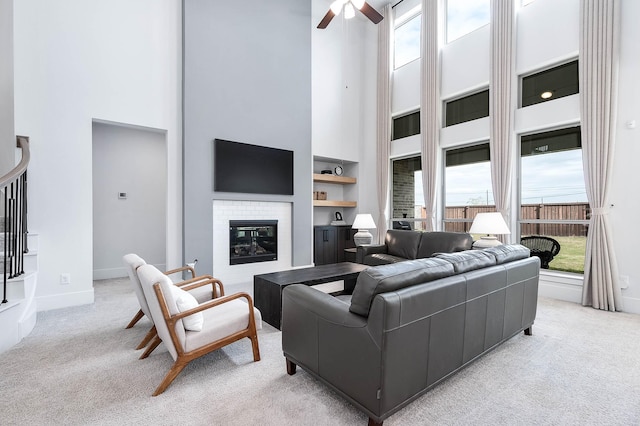 carpeted living room with a fireplace, a towering ceiling, built in features, and ceiling fan