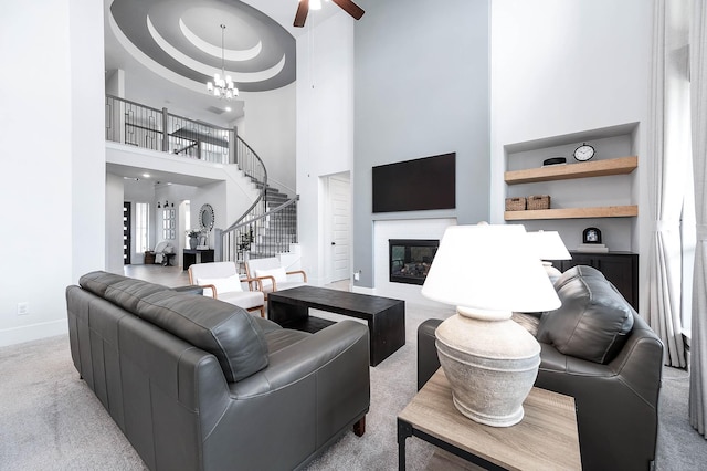 living room featuring light carpet, a towering ceiling, ceiling fan with notable chandelier, a tray ceiling, and built in features