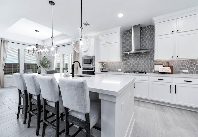 kitchen with a center island with sink, white cabinetry, wall chimney exhaust hood, and sink