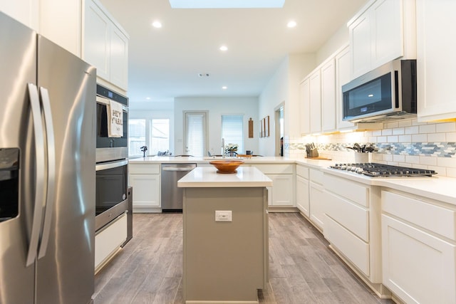 kitchen with kitchen peninsula, stainless steel appliances, white cabinets, hardwood / wood-style floors, and a center island