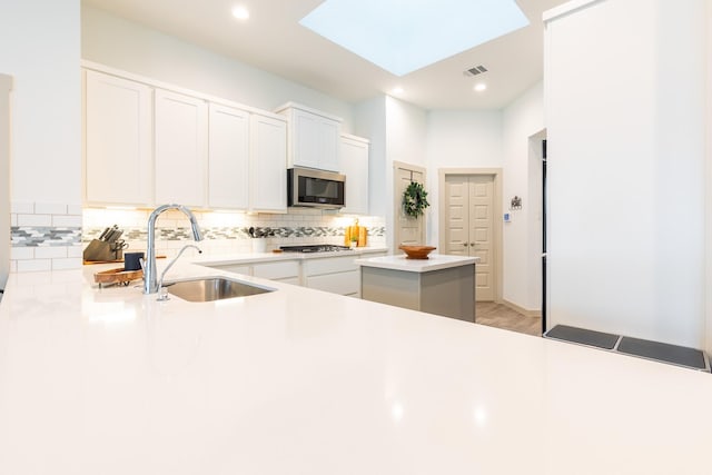 kitchen with a skylight, sink, white cabinets, and appliances with stainless steel finishes