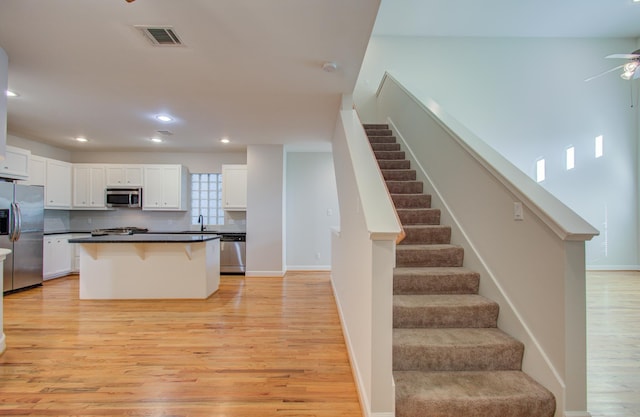 kitchen with a center island, white cabinets, light wood-type flooring, appliances with stainless steel finishes, and a breakfast bar area