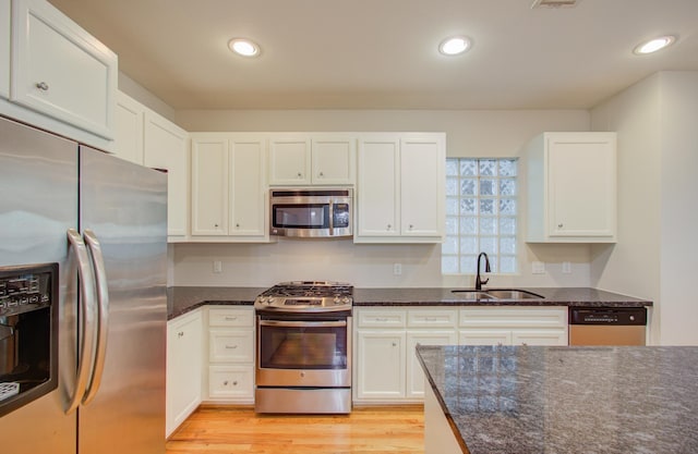 kitchen featuring sink, light hardwood / wood-style flooring, dark stone countertops, appliances with stainless steel finishes, and white cabinetry