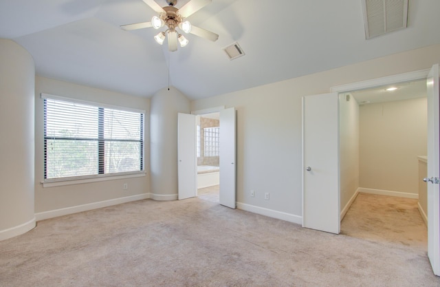 unfurnished bedroom featuring ceiling fan, light colored carpet, lofted ceiling, and ensuite bath