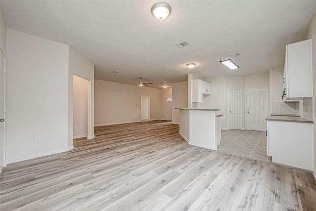 unfurnished living room with ceiling fan, a textured ceiling, and light hardwood / wood-style flooring