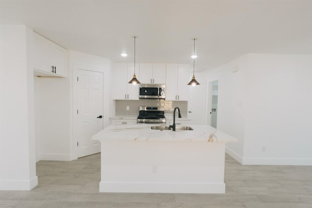 kitchen with light stone countertops, sink, stainless steel appliances, pendant lighting, and a kitchen island with sink