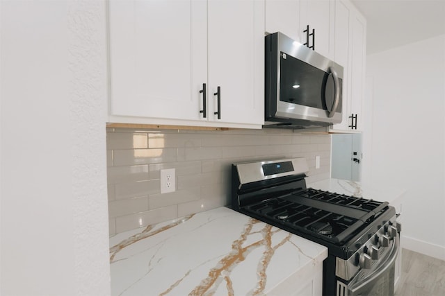 kitchen featuring backsplash, stainless steel appliances, light stone counters, and white cabinetry