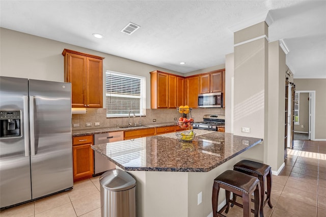 kitchen featuring dark stone counters, sink, light tile patterned floors, appliances with stainless steel finishes, and a kitchen island