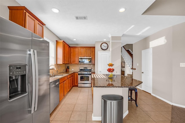 kitchen featuring stainless steel appliances, sink, dark stone countertops, a kitchen island, and light tile patterned flooring