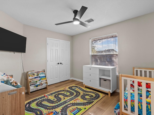 bedroom with hardwood / wood-style flooring, ceiling fan, a crib, and a closet