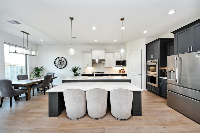 kitchen with decorative light fixtures, a kitchen island with sink, and appliances with stainless steel finishes