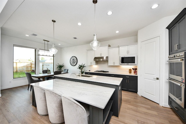 kitchen with stainless steel appliances, a kitchen island with sink, sink, pendant lighting, and white cabinetry