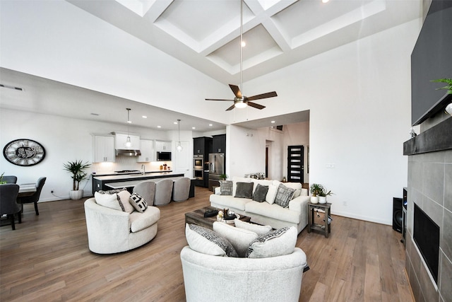 living room with dark hardwood / wood-style flooring, a towering ceiling, coffered ceiling, ceiling fan, and a fireplace