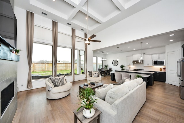 living room featuring coffered ceiling, ceiling fan, a healthy amount of sunlight, and light hardwood / wood-style flooring