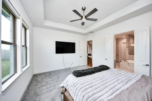 carpeted bedroom with multiple windows, connected bathroom, a raised ceiling, and ceiling fan