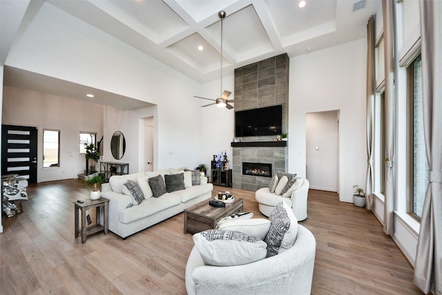 living room with a tiled fireplace, ceiling fan, a towering ceiling, and light hardwood / wood-style floors