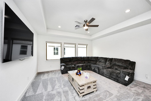 carpeted living room with a raised ceiling and ceiling fan