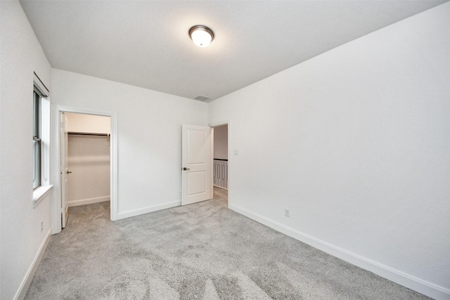 unfurnished bedroom featuring a walk in closet, a closet, and light colored carpet