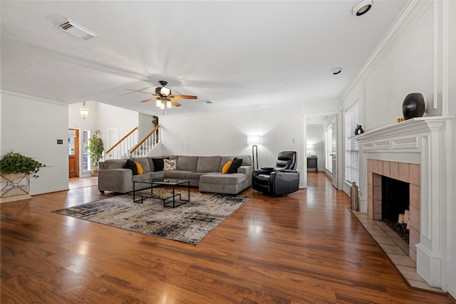 living room featuring hardwood / wood-style flooring, ceiling fan, ornamental molding, and a tiled fireplace