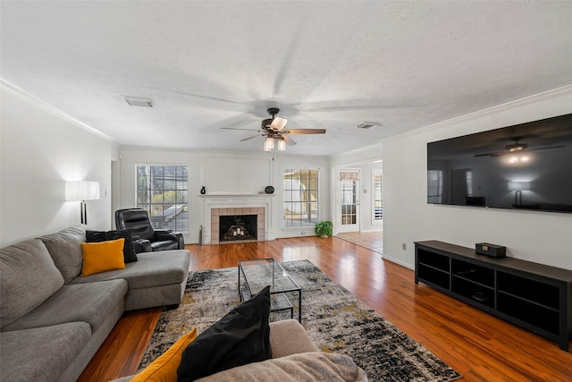 living room featuring crown molding, hardwood / wood-style flooring, ceiling fan, a fireplace, and a textured ceiling