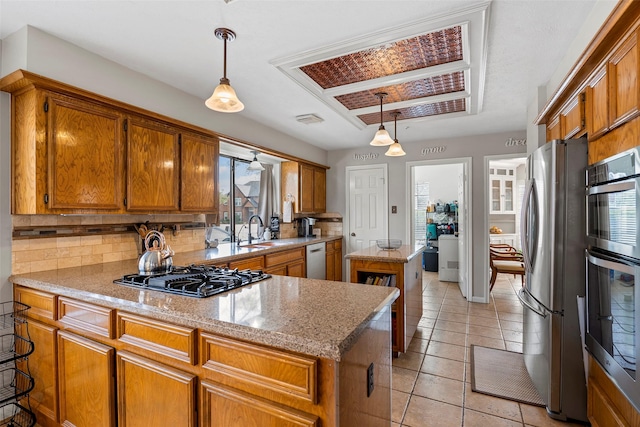 kitchen featuring sink, appliances with stainless steel finishes, hanging light fixtures, light stone counters, and a kitchen island