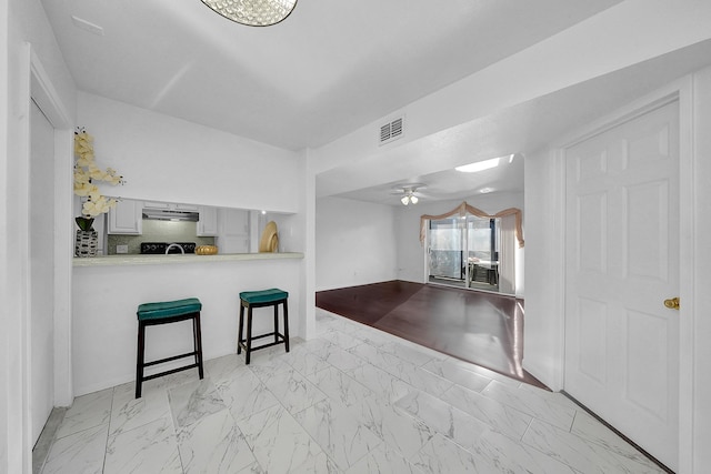 kitchen with kitchen peninsula, tasteful backsplash, a breakfast bar, ceiling fan, and white cabinets