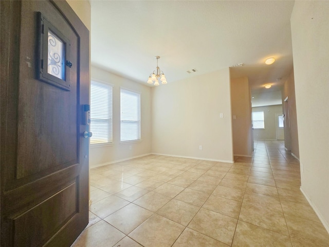 tiled empty room with a healthy amount of sunlight and an inviting chandelier