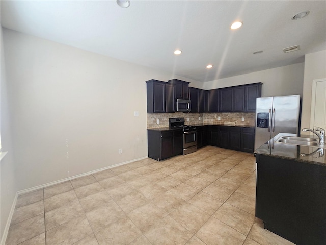 kitchen with sink, tasteful backsplash, dark stone counters, light tile patterned flooring, and appliances with stainless steel finishes