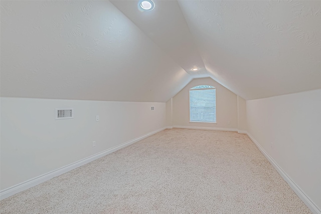 bonus room with a textured ceiling, light colored carpet, and lofted ceiling