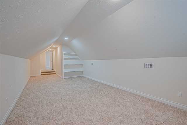 bonus room featuring a textured ceiling, light colored carpet, and built in features