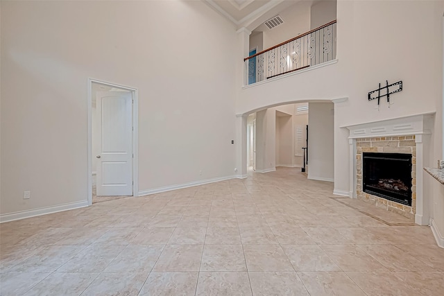 unfurnished living room featuring light tile patterned floors, a towering ceiling, a stone fireplace, and crown molding