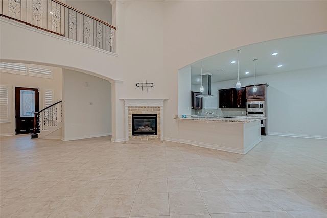 living room featuring a tile fireplace, sink, a towering ceiling, and light tile patterned flooring