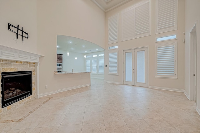 unfurnished living room with a tiled fireplace, french doors, light tile patterned floors, and a high ceiling