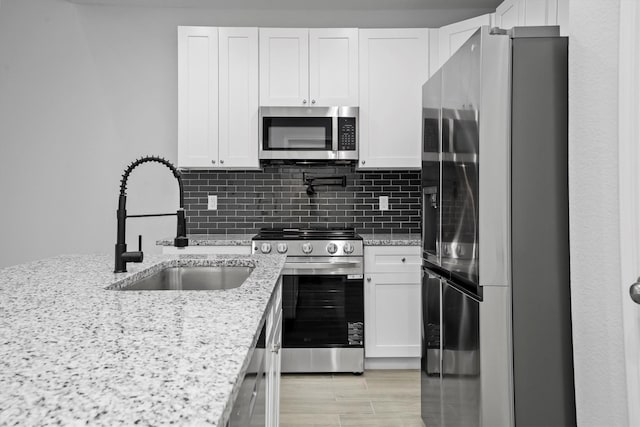 kitchen with appliances with stainless steel finishes, tasteful backsplash, light stone countertops, white cabinets, and sink