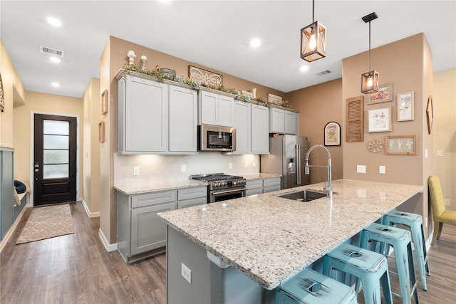 kitchen with pendant lighting, backsplash, light stone countertops, appliances with stainless steel finishes, and a kitchen bar