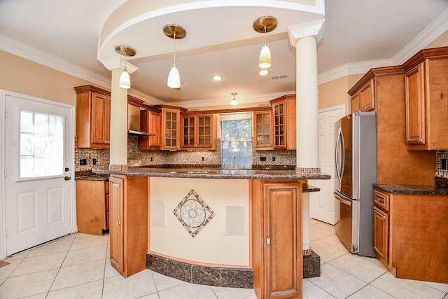 kitchen featuring ornate columns, dark stone countertops, stainless steel fridge, decorative light fixtures, and ornamental molding