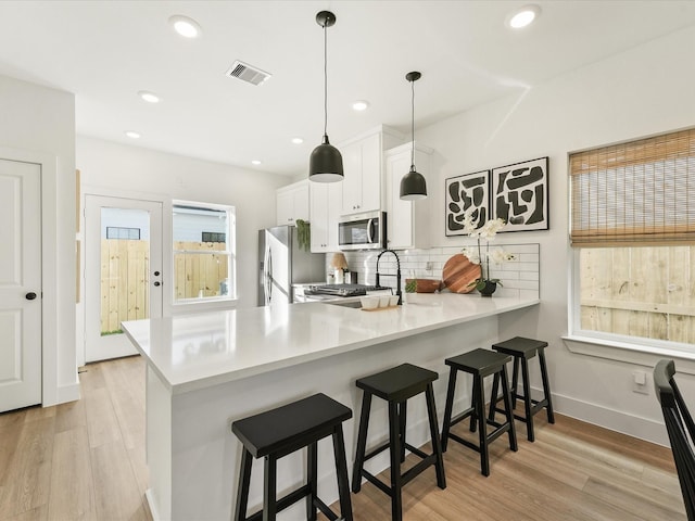 kitchen with white cabinetry, hanging light fixtures, stainless steel appliances, kitchen peninsula, and a kitchen bar