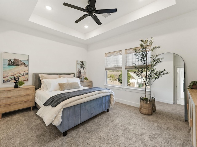 carpeted bedroom with a raised ceiling and ceiling fan