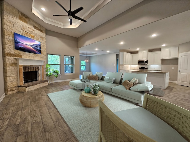 living room with a tray ceiling, ceiling fan, crown molding, hardwood / wood-style flooring, and a stone fireplace