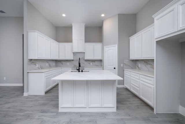 kitchen with backsplash, light wood-type flooring, white cabinetry, and an island with sink