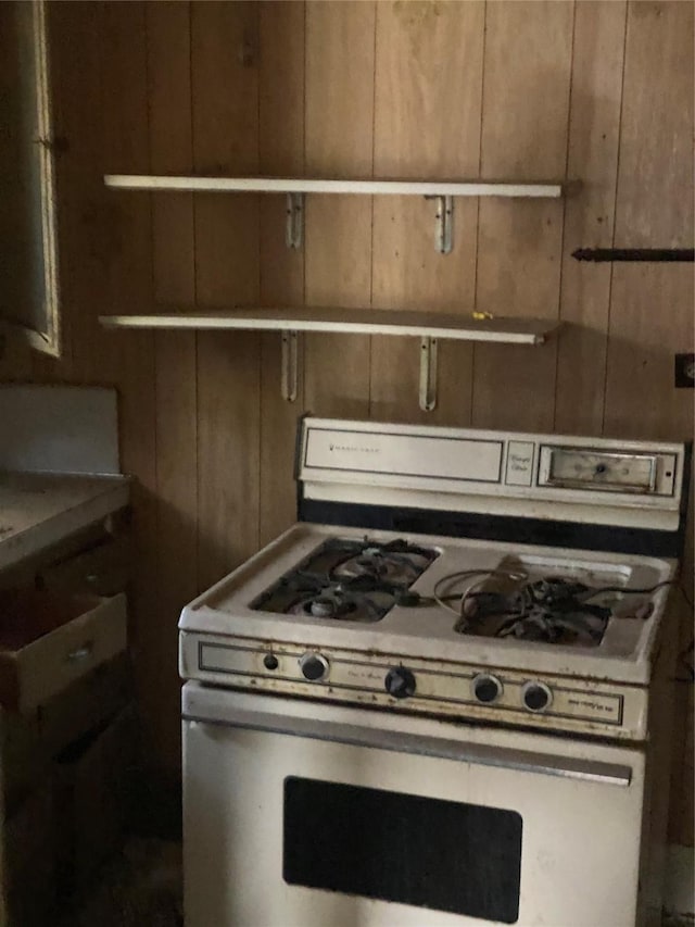 kitchen featuring white range with gas stovetop and wood walls