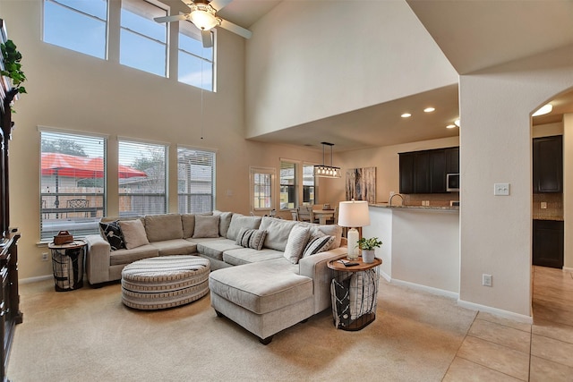 living room featuring light tile patterned floors, sink, ceiling fan, and a high ceiling