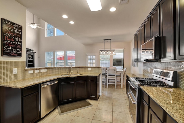 kitchen with appliances with stainless steel finishes, light stone counters, dark brown cabinetry, sink, and pendant lighting