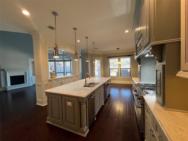 kitchen with appliances with stainless steel finishes, dark hardwood / wood-style floors, sink, hanging light fixtures, and a kitchen island with sink